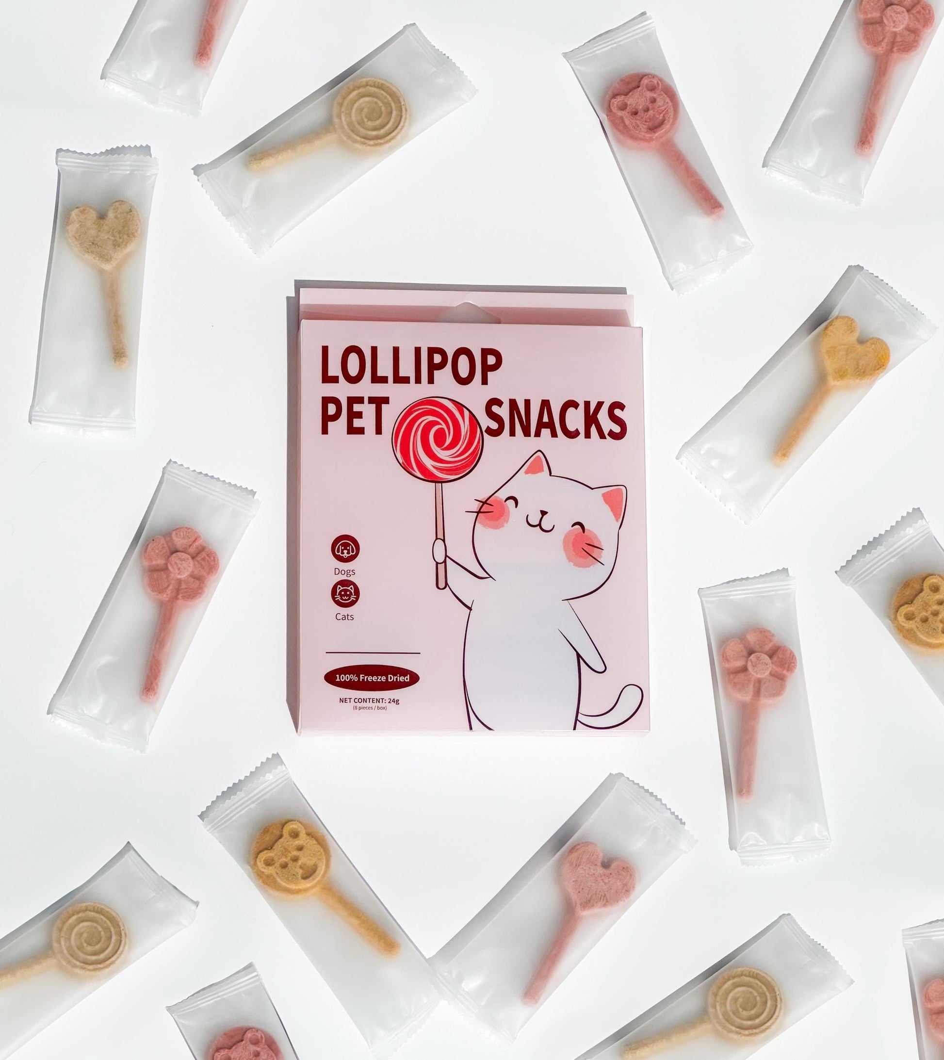 A box of lollipop pet snacks with a cartoon cat holding a red lollipop. The box is pink with white text that reads 'Lollipop Pet Snacks'. The box is surrounded by individual packages of the snacks, which are in various shapes, including hearts, flowers, bears and lollipops. The snacks are in different colors, including pink, red, and yellow. The text on the box also reads 100% Freeze Dried.