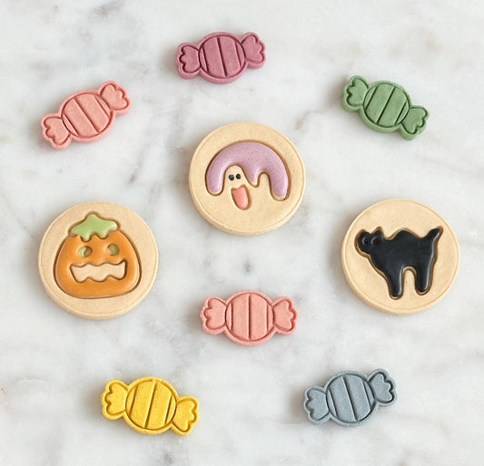 Set of colorful frosted Pilsbury Halloween cookie pet treats of a pumpkin, ghost and cat with candy designed pet treats on marble surface