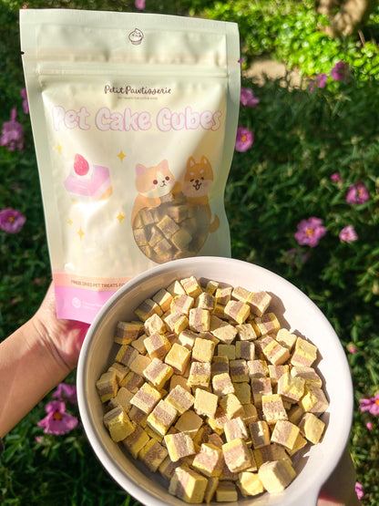 The bag of pet cake cubes is in the background and has a pink and white design with the words &#39;Petit Pawtisserie&#39; and &#39;Pet Cake Cubes&#39;. Petit Pawtisserie freeze-dried cake cube pet treats for cats and dogs – soft bite sized snacks with 3 layers of flavor